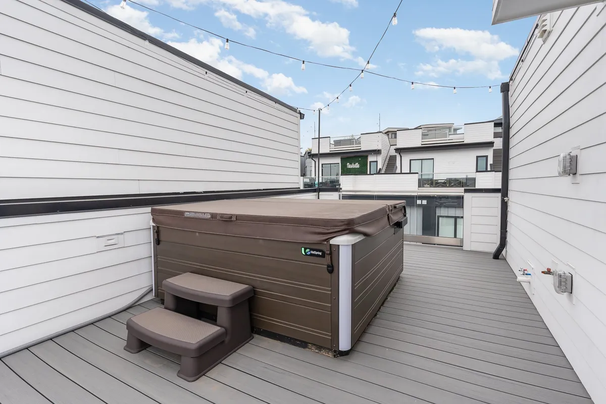 This image presents a rooftop deck featuring a private hot tub surrounded by string lights and a stylish deck area. The city skyline can be glimpsed in the background, evoking the spirit of Nashville's nightlife and offering a taste of the evening ambiance guests can enjoy before heading out.