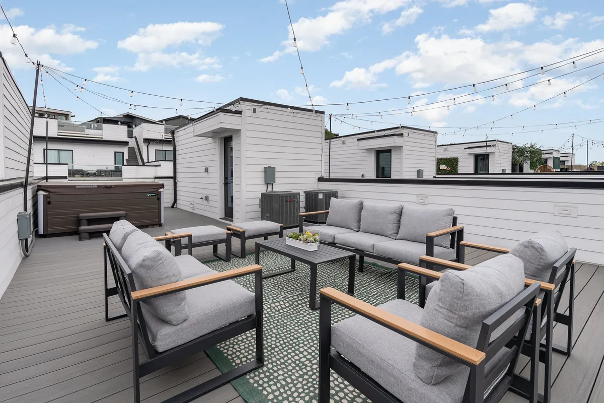 An inviting rooftop space featuring a hot tub, outdoor seating, and festive string lights. The relaxed, sociable vibe and open-air environment evoke pre-night-out gatherings and sunset celebrations.