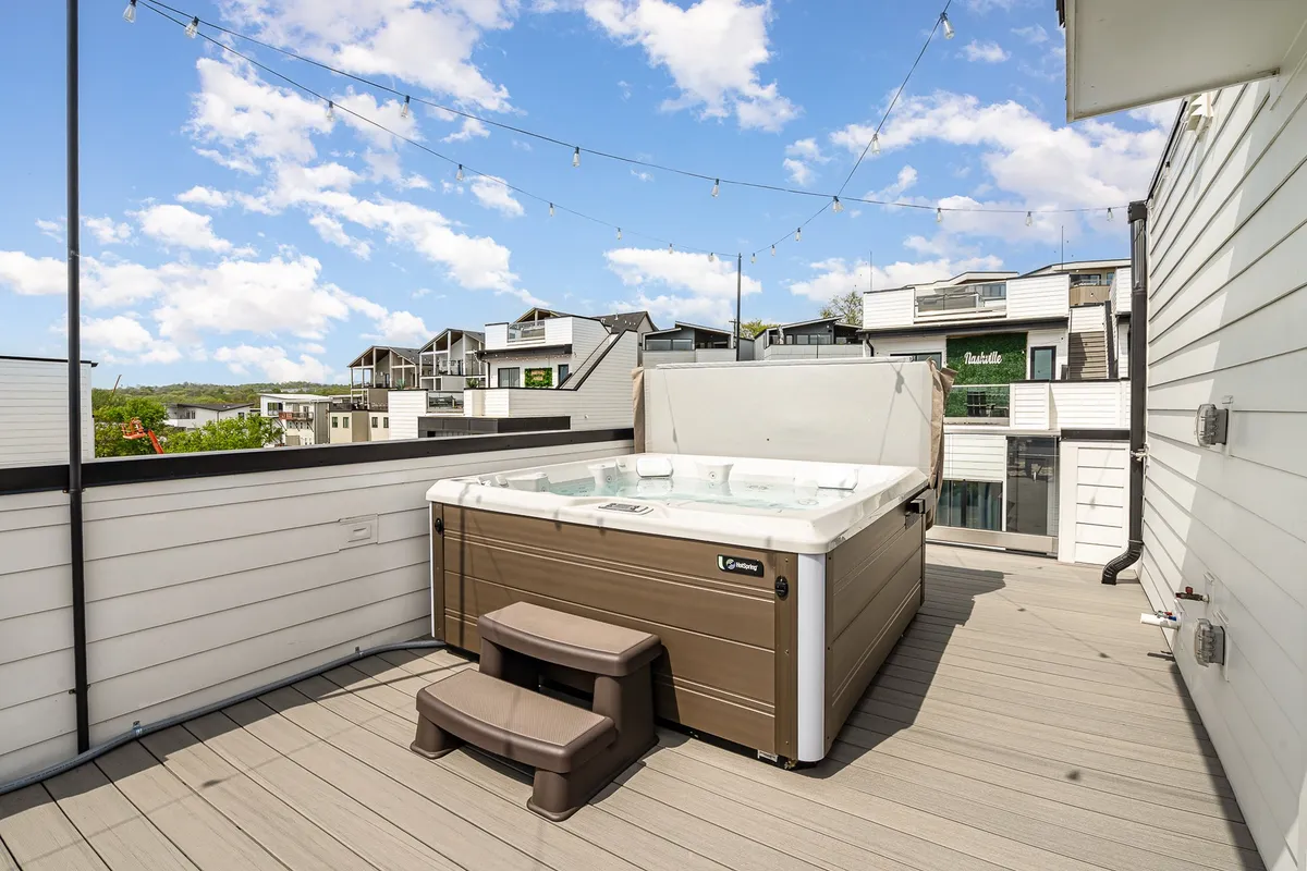 A stylish rooftop deck with a hot tub, deck seating, and string lights, framed by surrounding city views. The space is designed for relaxation, group fun, and taking in the Nashville skyline, making it ideal for winding down after a day exploring local attractions.