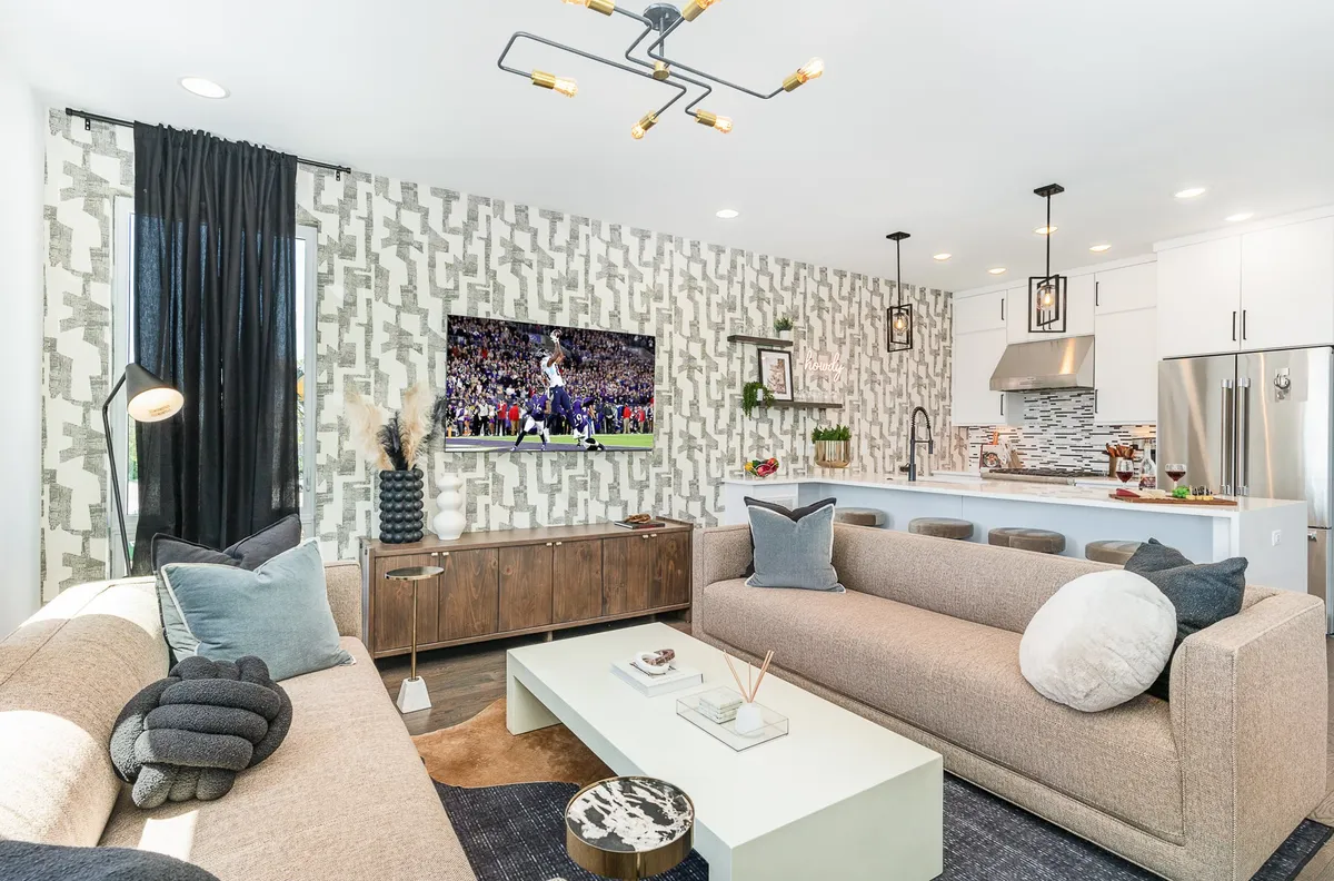 A contemporary living room setup with comfortable sofas arranged to encourage conversation and togetherness. A stylish coffee table anchors the space, and a large television displays a sports event, suggesting energy and excitement. The room appears spacious and modern, with subtle décor touches that make it inviting for both casual and festive occasions.