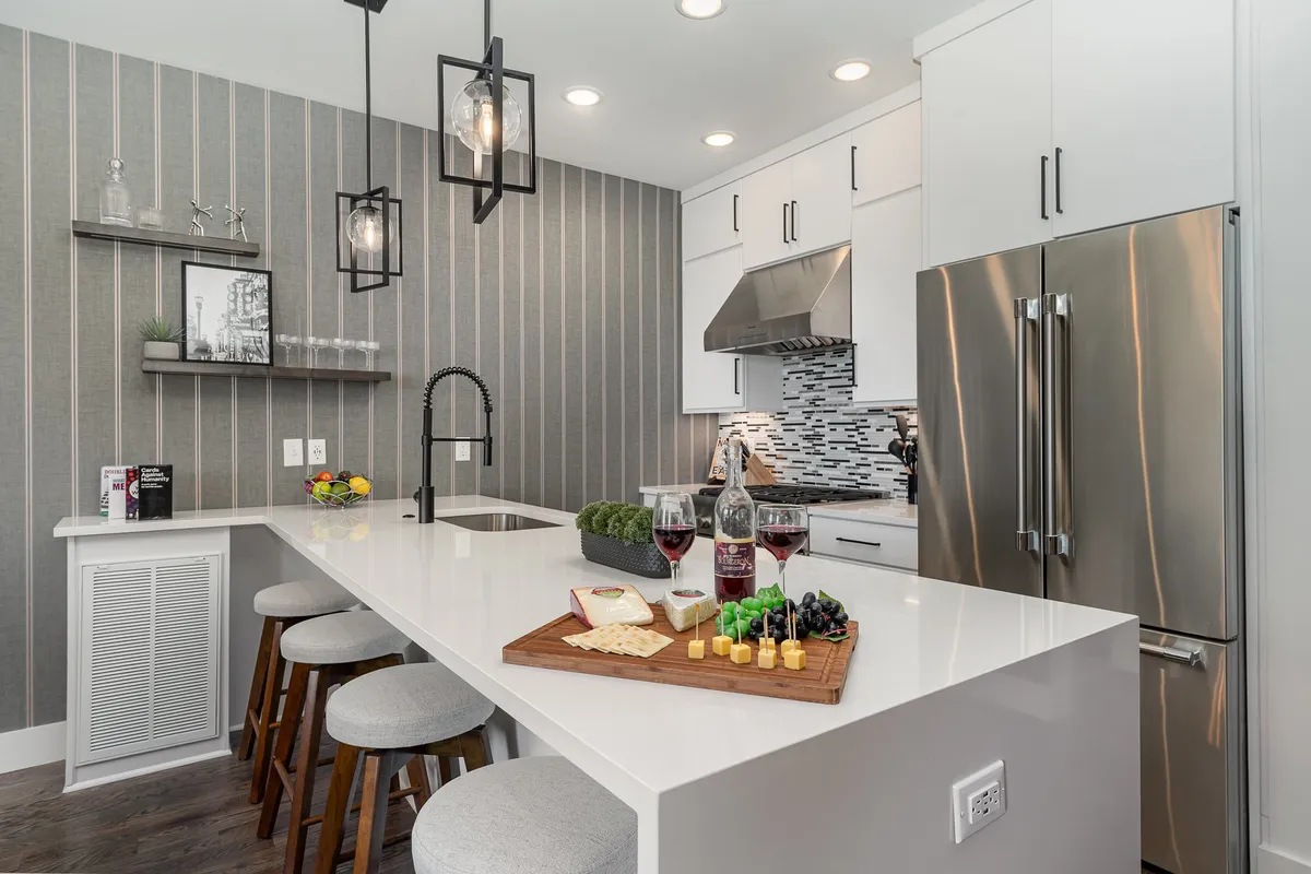 A cozy, inviting kitchen with a central island, gourmet cheese platter, and elegant hanging light fixtures. The kitchen exudes warmth and sophistication, with the island acting as a hub for food preparation, entertaining, and socializing over wine.