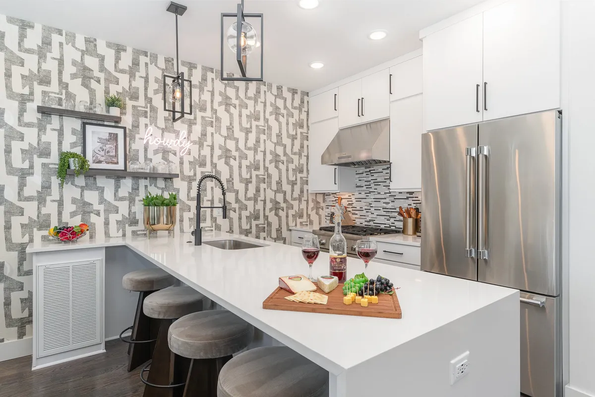 A modern kitchen island set for entertaining, featuring wine glasses and a cheese board. The inviting atmosphere suggests a space for group meals, casual brunches, or celebratory toasts. Kitchen appliances and warm lighting add to the communal feel.