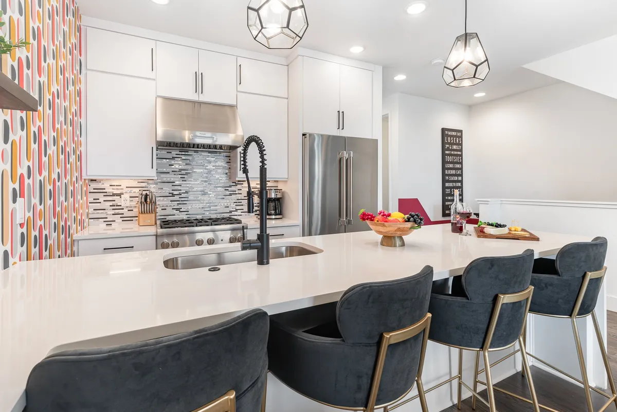 A bright, vibrant kitchen featuring a contemporary island, stylish bar stools, colorful accent wall, and gleaming appliances. The design is open and airy, making it ideal for gathering, cooking, and sharing meals with friends or family.