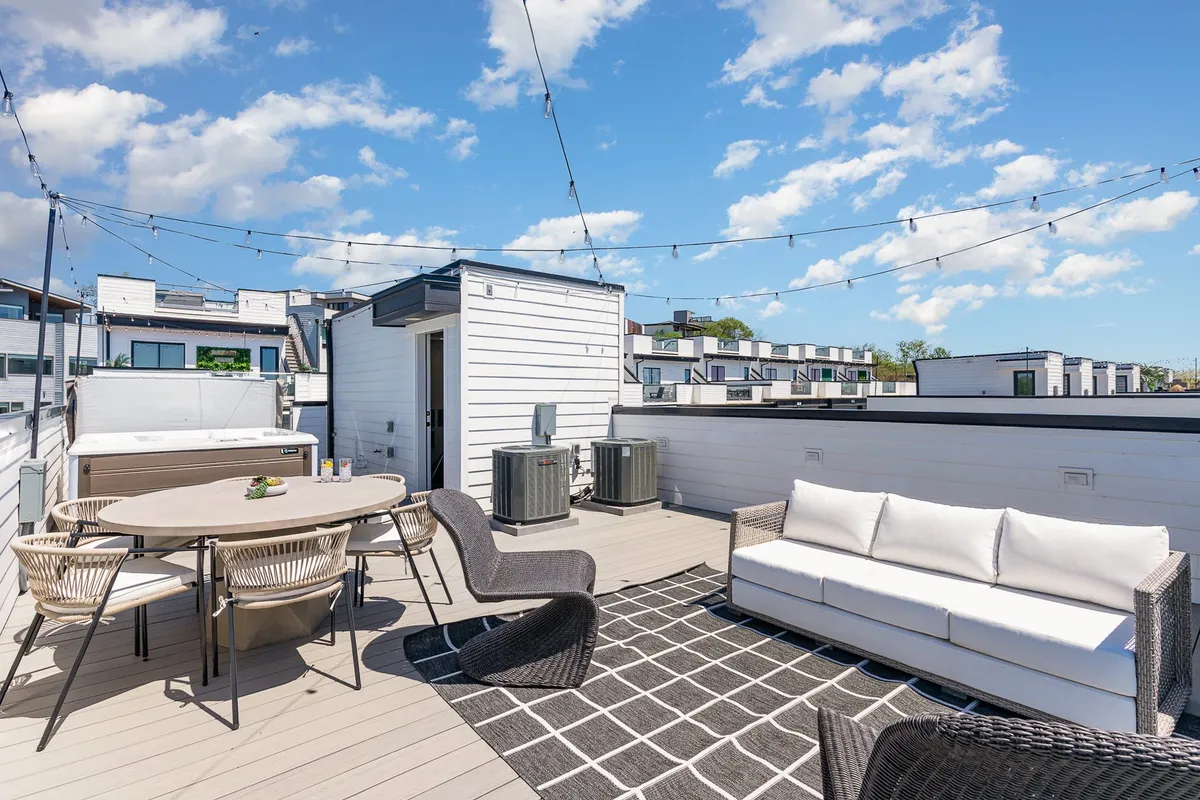 A rooftop deck set up for outdoor dining, with a spacious seating area, decorative string lights, and a large table ready for brunch or sunset cocktails. The soft glow of the lights creates a welcoming and festive mood.