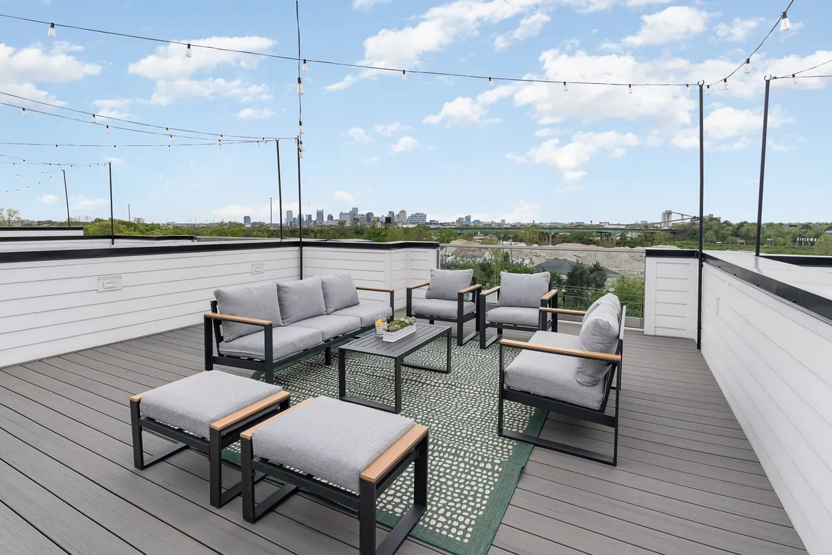 A vibrant rooftop scene with comfortable outdoor seating, glowing string lights, and a striking view of the Nashville city skyline. The setup encourages group gatherings, sunset viewing, and late-night conversations, reflecting the social energy of Nashville’s nightlife.