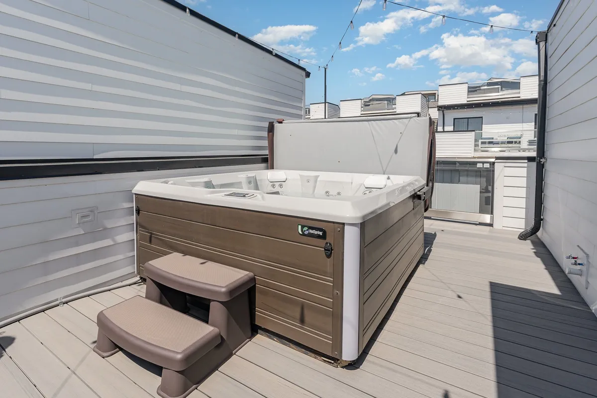 A tranquil rooftop featuring a modern hot tub with steps leading up, surrounded by soft evening light. The space feels intimate and ideal for soaking under the stars or unwinding after a day exploring the city.
